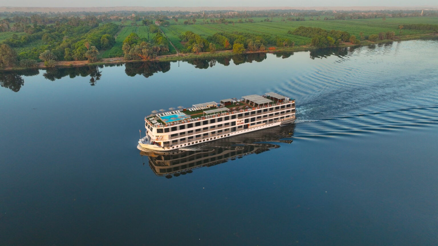 M/S City and Sea Adonis luxury Nile cruise ship sailing past lush green riverbanks and palm trees.