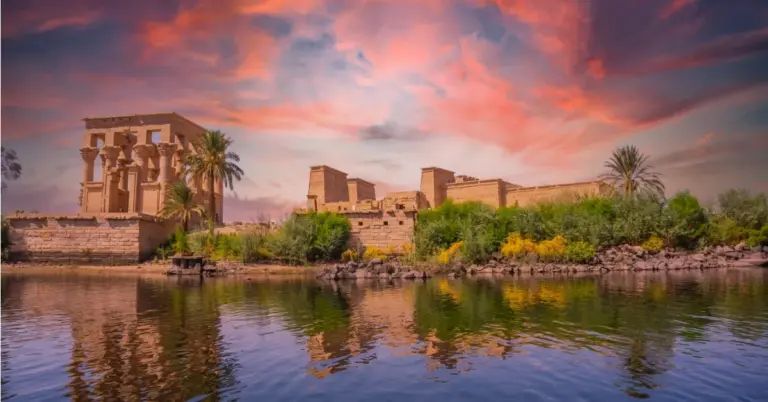 The Temple of Philae glows under a dramatic pink sunset sky, reflected in the calm Nile waters at Aswan.