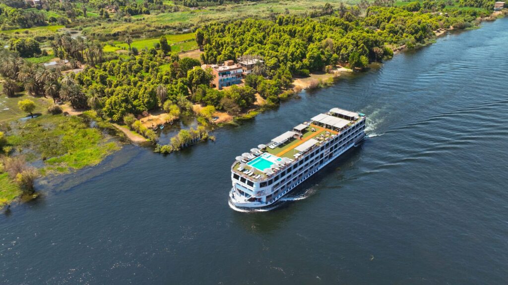 M/S City & Sea Adonis cruising the Nile River through lush green landscape and palm trees.