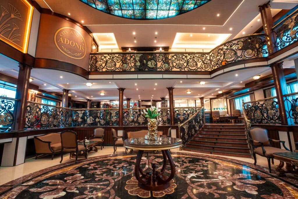 Elegant atrium lobby aboard the M/S City & Sea Adonis with ornate railings and central staircase.