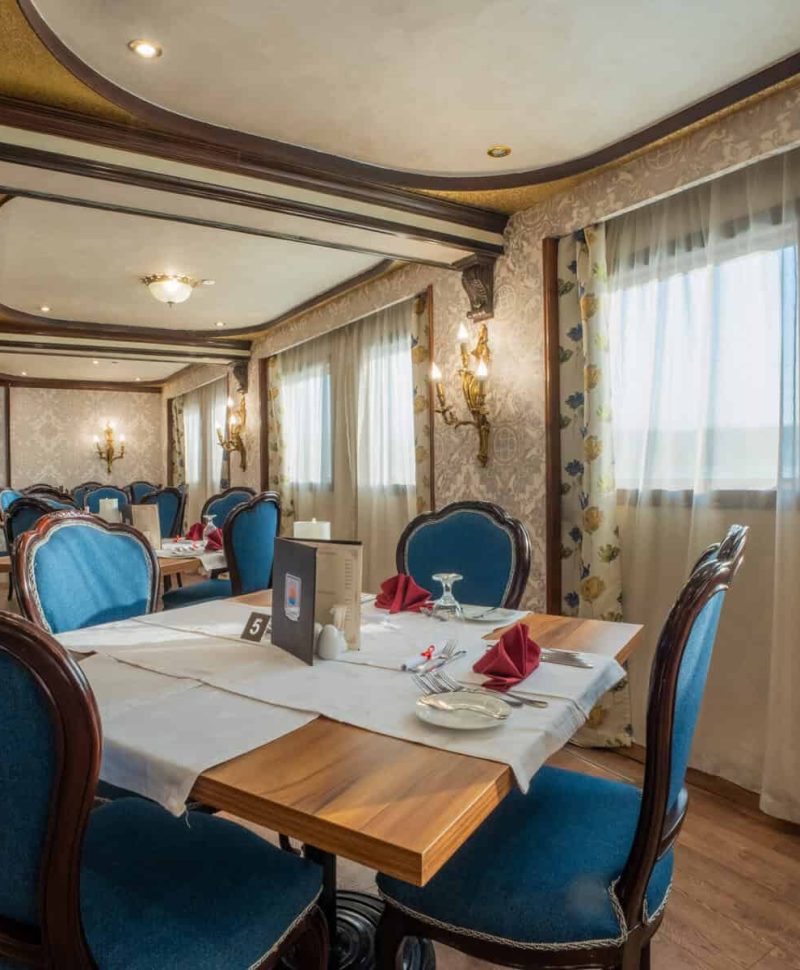 Elegant dining room aboard the M/S City & Sea Adonis with blue velvet chairs and river views.