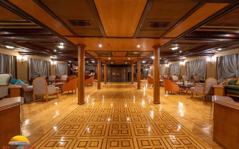 Spacious lounge aboard the M/S City & Sea Adonis with wooden ceiling, elegant seating and polished parquet flooring.