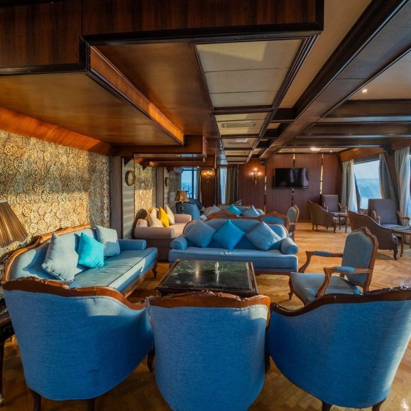 Elegant lounge aboard the M/S City & Sea Adonis with blue seating, ornate wallpaper and Nile River views.