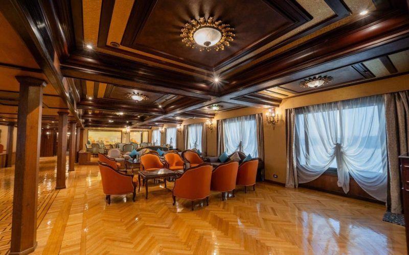 Elegant lounge aboard the M/S City & Sea Adonis with ornate ceiling, orange armchairs and large windows.