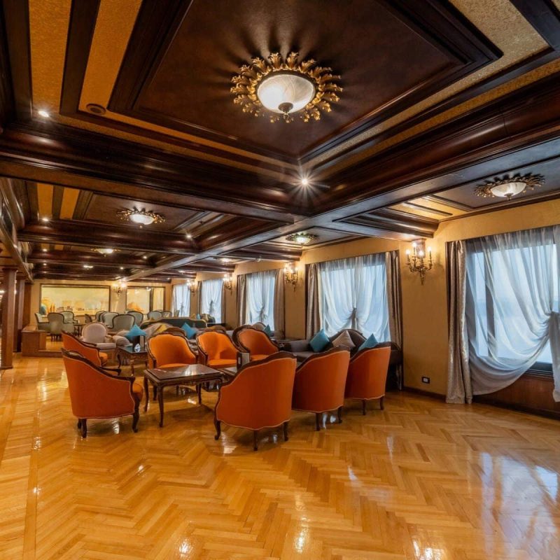 Elegant lounge aboard the M/S City & Sea Adonis with ornate ceiling, orange armchairs and large windows.
