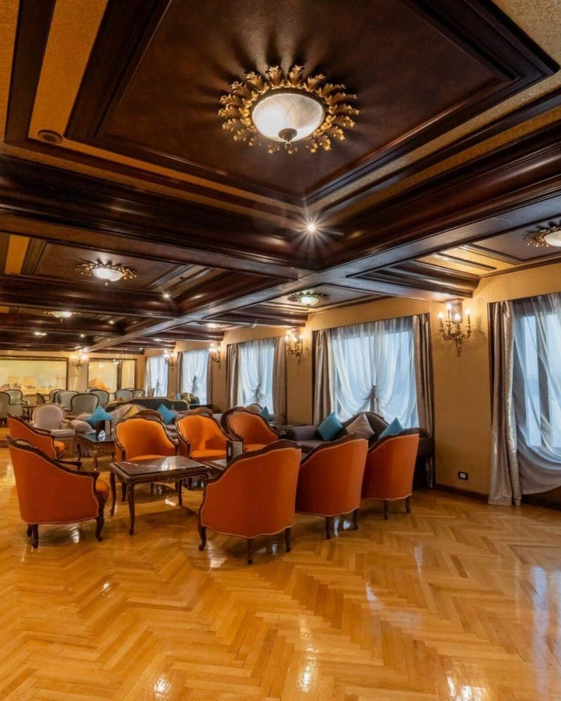 Elegant lounge aboard the M/S City & Sea Adonis with ornate ceiling, orange armchairs and large windows.