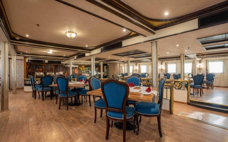 Elegant dining room aboard the M/S City & Sea Adonis with blue upholstered chairs and wooden tables.