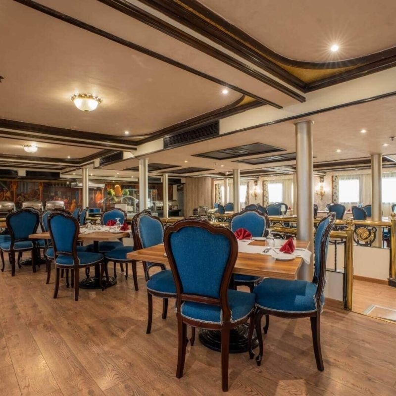 Elegant dining room aboard the M/S City & Sea Adonis with blue upholstered chairs and wooden tables.