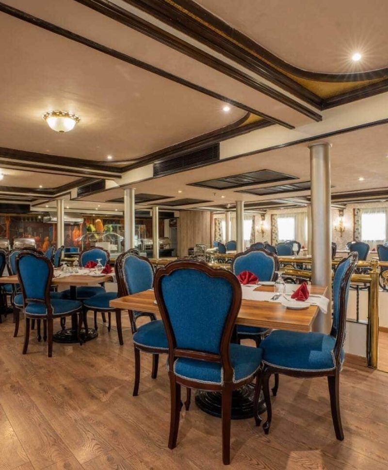 Elegant dining room aboard the M/S City & Sea Adonis with blue upholstered chairs and wooden tables.