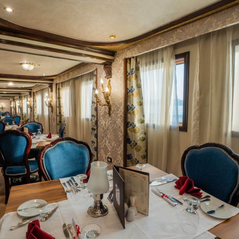 Elegant dining room aboard the M/S City & Sea Adonis with blue velvet chairs and river views.