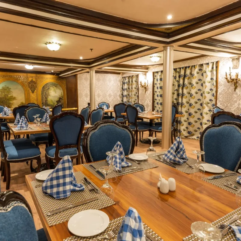Formal cruise ship dining room with elegant blue upholstered chairs, checkered tablecloths, and opulent wall art