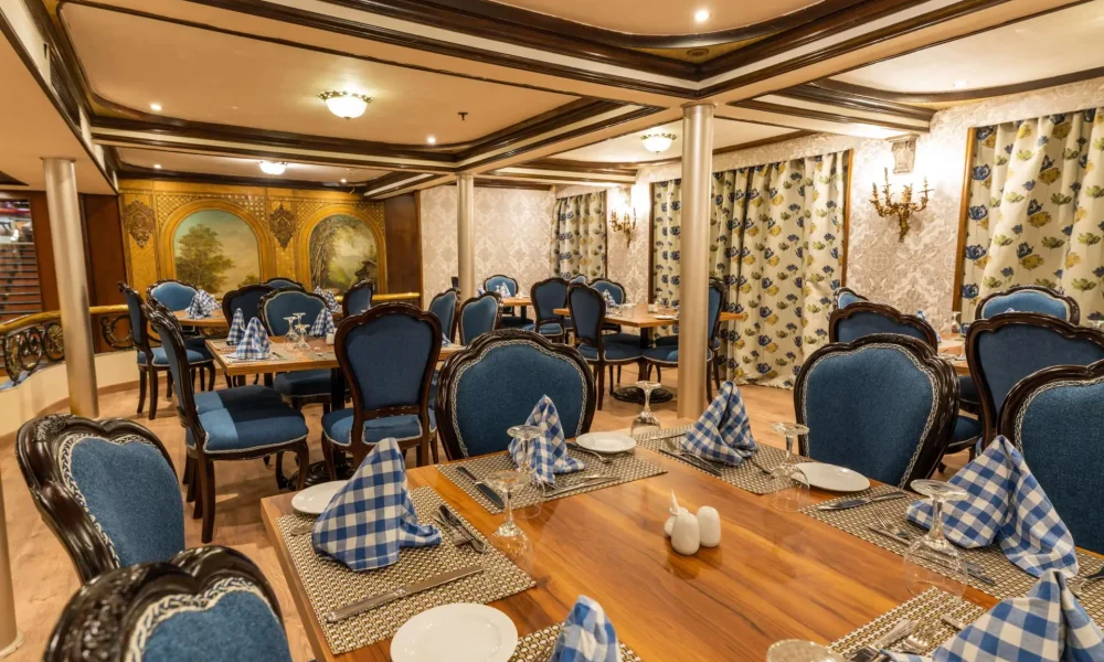 Formal cruise ship dining room with elegant blue upholstered chairs, checkered tablecloths, and opulent wall art