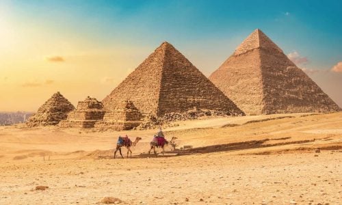 Bedouin with camels on a background of pyramids at sunset