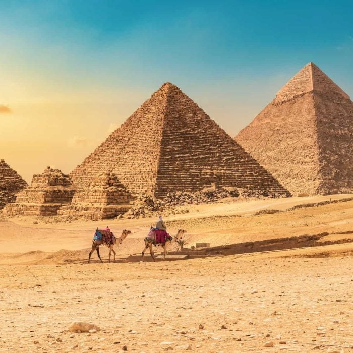 Bedouin with camels on a background of pyramids at sunset