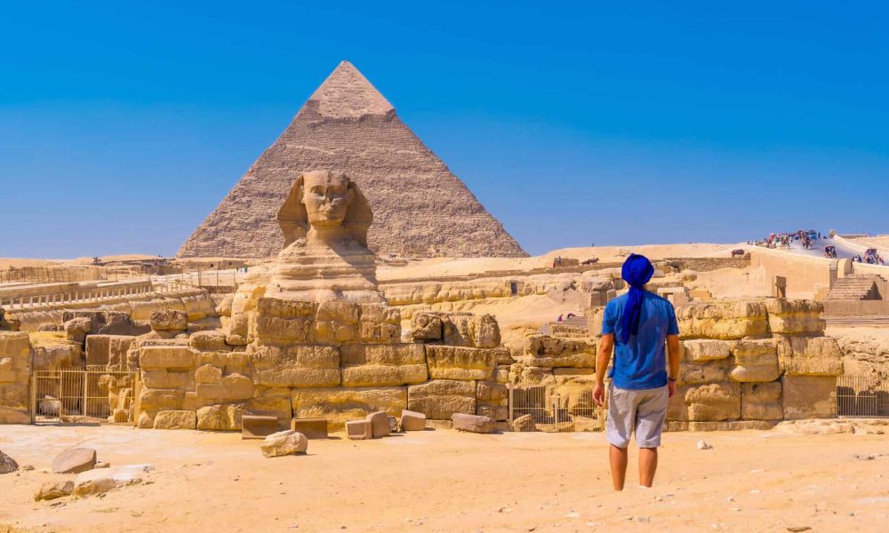 A young man walking towards the Great Sphinx of Giza and in the background the pyramid of Khafre,